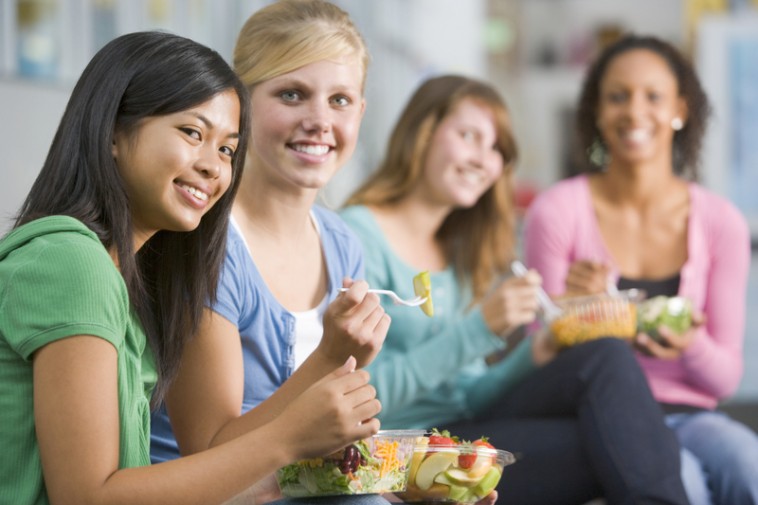 Four female students enjoying lunch together eating salads