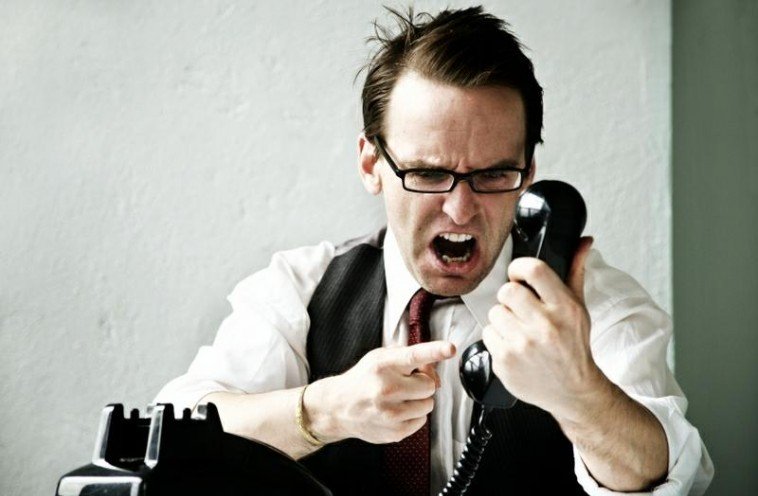 Male with glasses yelling into the phone and pointing at the receiver